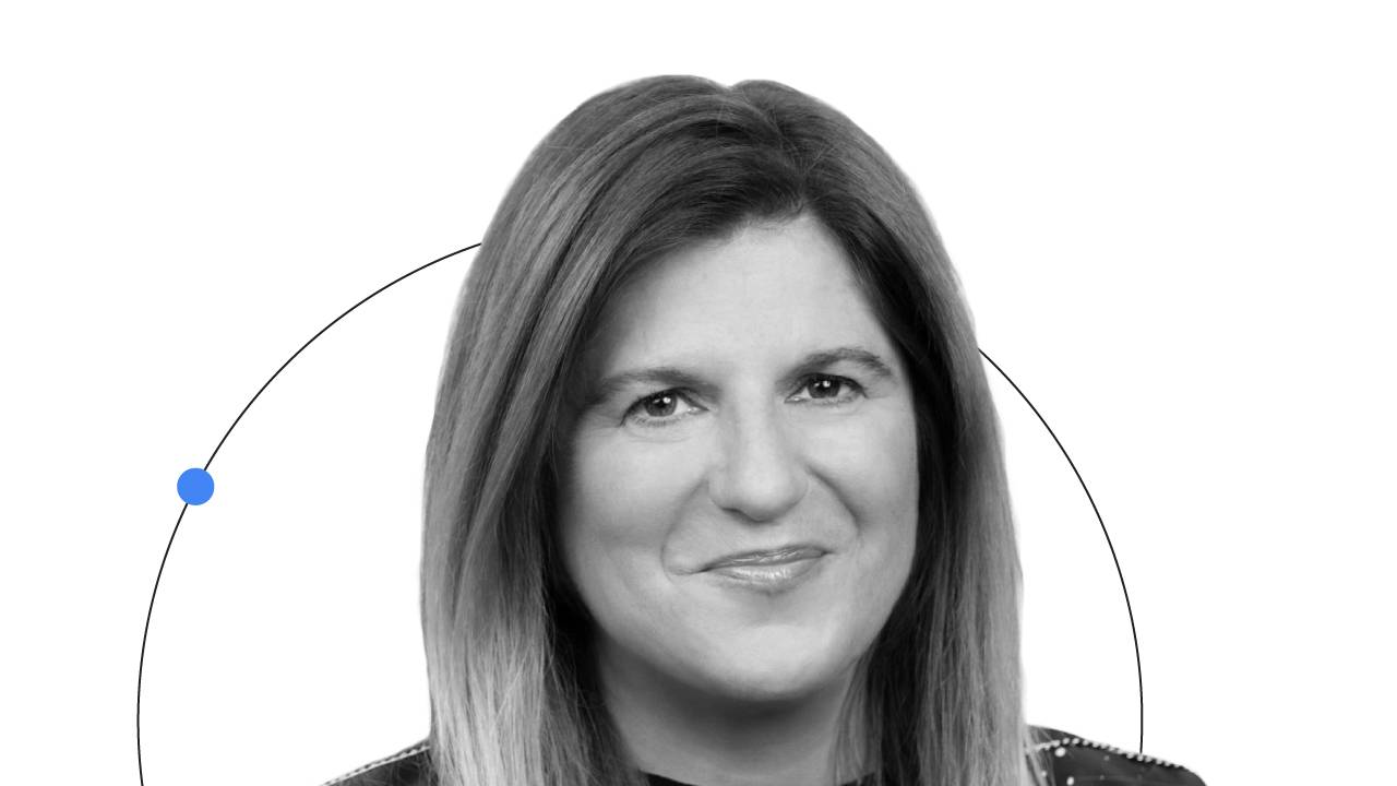 Un'immagine che ritrae Lorraine Twohill, CMO di Google, dalle spalle in su, mentre sorride. Twohill ha i capelli e la carnagione chiari e indossa un top nero. Sul suo viso c'è un circolo blu semitrasparente e dietro di lei c'è una linea che disegna un arc